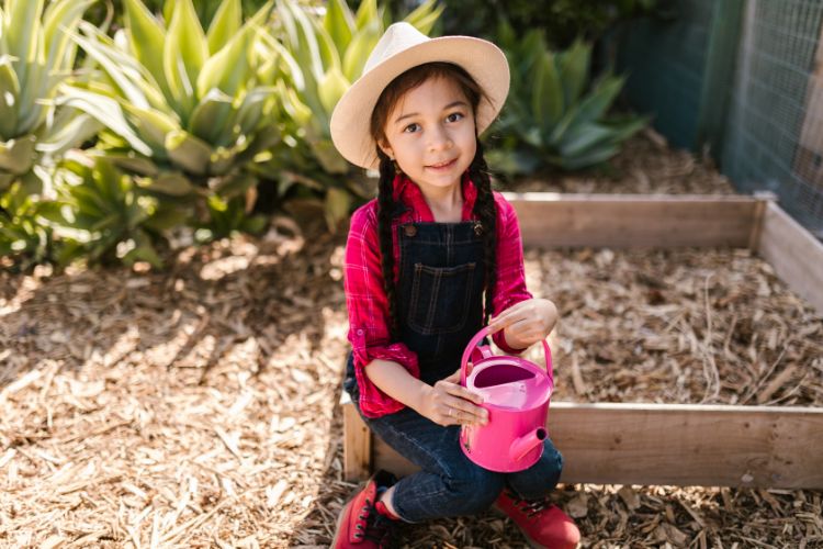 8 year old girl holding a watering can ready to garden as part of her chores
